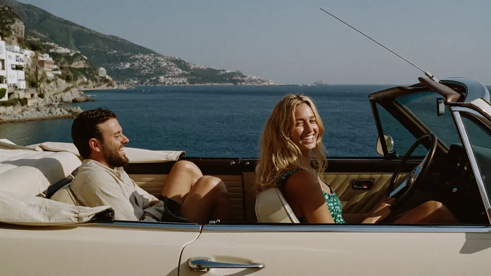 Two adult friends in a convertible beside the Italian coast